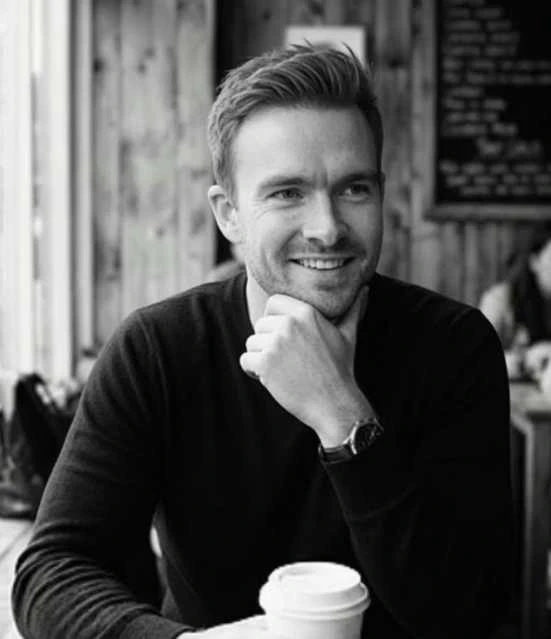 Richard in a black and white photograph, smiling and leaning on his hand