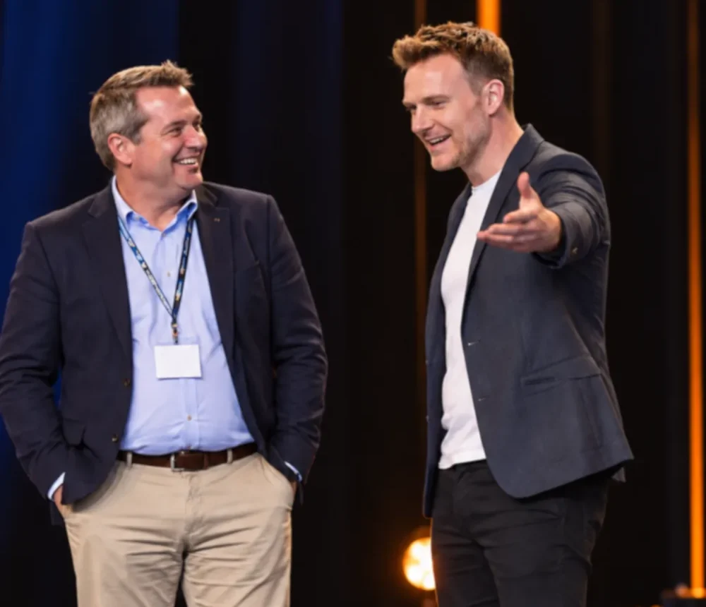 Two men talking on a stage, one gesturing out to the audience
