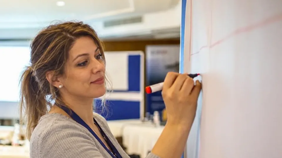 A woman smiling as she writes on a flip chart during a workshop