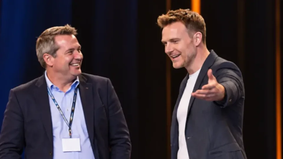 Richard on stage with a senior leader, gesturing out to the audience
